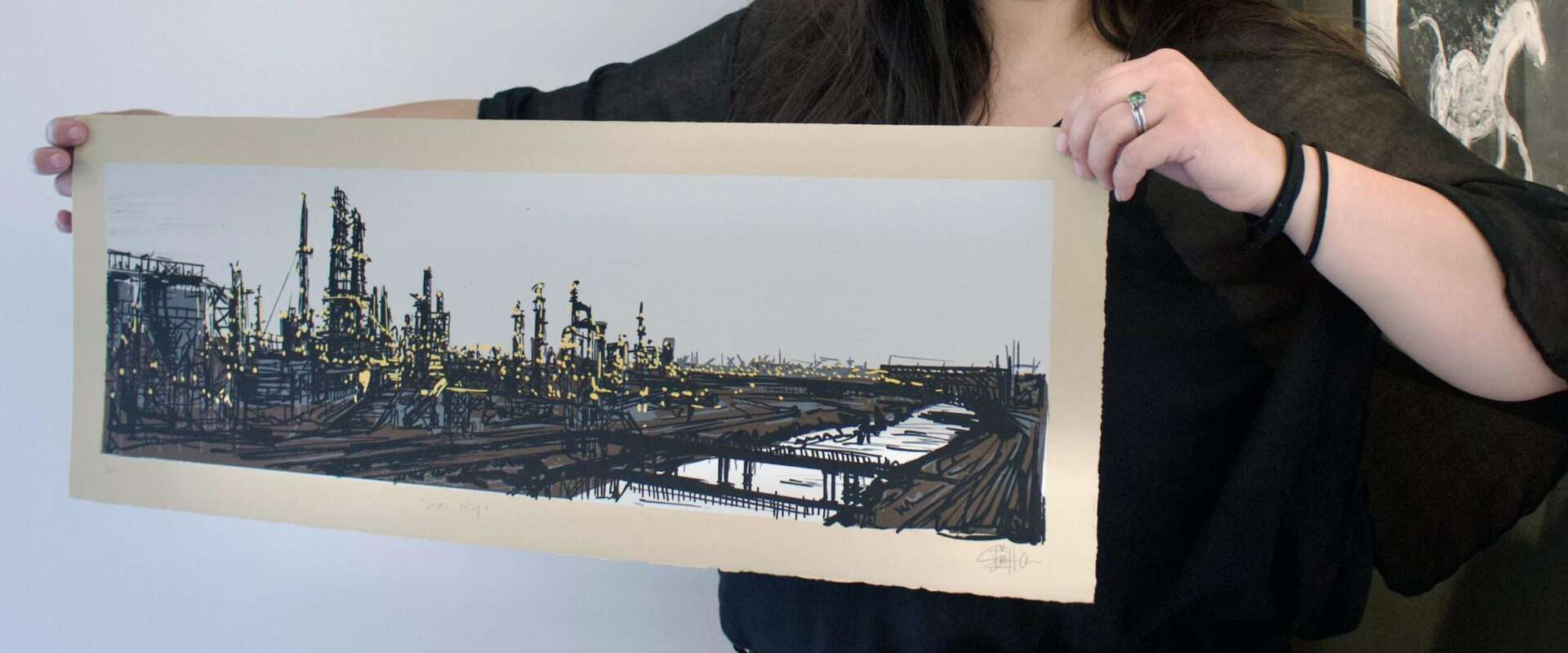 Hands holding a screen print of an oil refinery